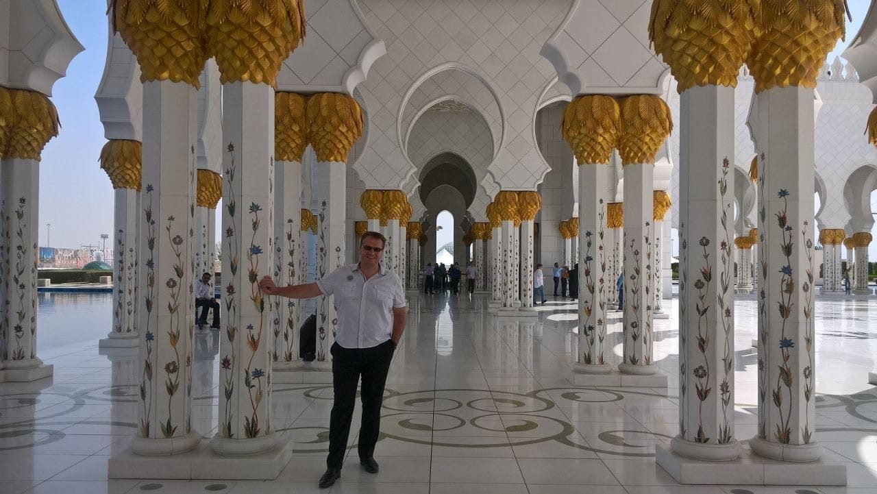 Radim Kaufmann in the colonnade of the Sheikh Zayed Grand Mosque in Abu Dhabi, with floral inlaid marble columns and golden palm-leaf capitals